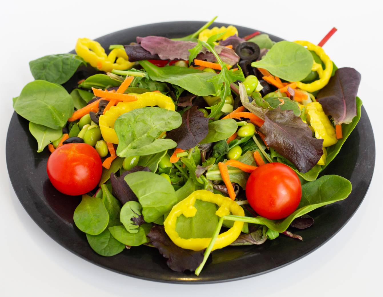 A photograph of a bowl of salad with spinach, cherry tomatoes, carrots, and banana peppers.